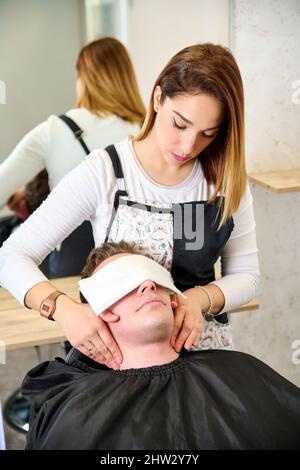 Friseur legte ein heißes Handtuch auf das Gesicht des Mannes, bevor er sich im Friseurladen rasieren konnte Stockfoto
