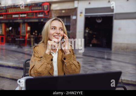 Schöne Dame, die am Tisch in der Nähe des Cafés sitzt und mit dem Smartphone anruft Stockfoto