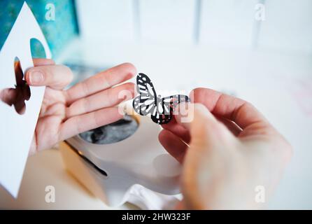 Die richtigen Werkzeuge zum Basteln. Kurzer Schuss einer Frau mit Händen, die einen ausgestanzten Papierschmetterling in der Hand hält. Stockfoto