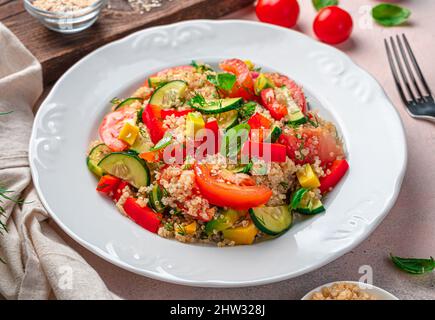 Gesunder Gemüsesalat mit Quinoa und frischen Kräutern auf grauem Hintergrund. Seitenansicht, Nahaufnahme. Stockfoto