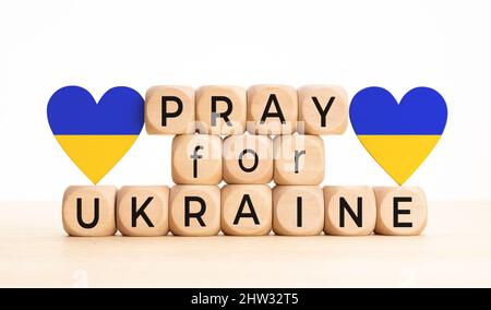 Betet für die Botschaft der Ukraine auf Holzblöcken und die Flagge der Ukraine in Herzform Stockfoto