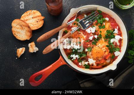 Shakshuka. Hausgemachte Spiegeleier mit Gemüse in eiserner Pfanne auf altem dunklen Schiefer, Stein oder Beton Hintergrund. Traditionelle Küche Israels. Spät Stockfoto