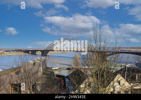 Nijmegen (Waalbrug), Niederlande - Februar 27. 2022: Blick vom Hügel über den Fluss waal auf einer Stahlbogenbrücke mit zwei Pylonen gegen den blauen Winterhimmel Stockfoto