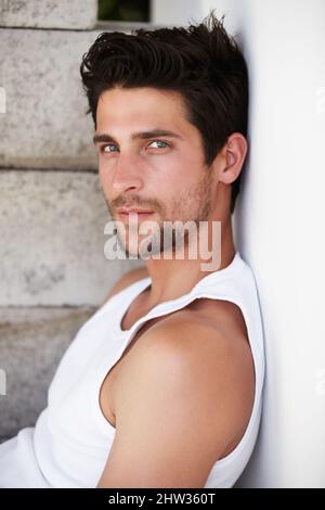 Schön in Ruhe. Ein hübscher junger Mann starrt Sie an, während er sich an eine Wand lehnt. Stockfoto