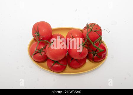 Nahaufnahme von roten reifen Tomaten auf orangefarbenem Tablett auf weißem Tisch Stockfoto