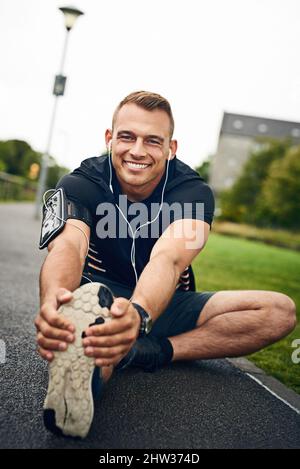 Machen Sie einen Unterschied, indem Sie die Distanz zurücklegen. Porträt eines sportlichen jungen Mannes, der sich vor einem Lauf im Freien dehnt. Stockfoto