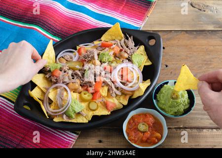 Hände, die Nahrung aus einem Tablett Nachos mit Fleisch nehmen. Schüsseln mit Salsa. Speicherplatz kopieren. Mexikanisches Küchenkonzept. Stockfoto