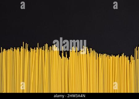 Rahmen aus ungekochten italienischen Spaghetti mit Platz für Text, Nahaufnahme, Textur von gelben rohen langen Nudeln auf schwarzem Hintergrund Stockfoto