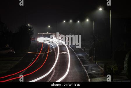 Streifen von Autoscheinwerfern und Heckleuchten, während sie nachts unter der Straßenbeleuchtung, Worcestershire, England, eine Wohnstraße entlang fahren. Stockfoto