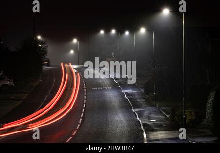 Streifen von Autoscheinwerfern und Heckleuchten, während sie nachts unter der Straßenbeleuchtung, Worcestershire, England, eine Wohnstraße entlang fahren. Stockfoto