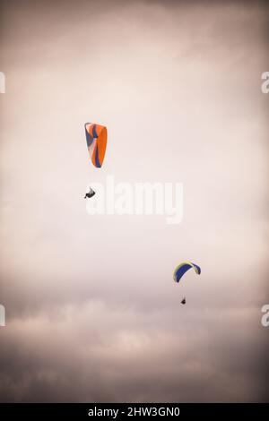 Bild von einigen Gleitschirmfliegern, gegen einen grau bewölkten Himmel. Stockfoto