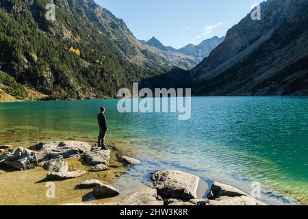 Der junge Reisende tritt auf Felsen am Ufer des Lac de Gaube in den französischen Pyrenäen Stockfoto