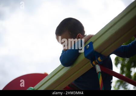 Kind stieg hoch auf Treppen. Vorschulkinder kletterten auf den Spielplatz. Junge spielt gefährlich im Kinderbereich im Hof. Stockfoto