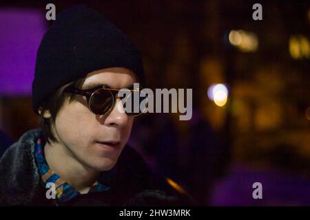 Typ mit schwarzer Brille und schwarzem Hut. Porträt eines Mannes in der Nähe der Bar. Junger Mann in künstlichem Licht. Student bei Nacht. Stockfoto