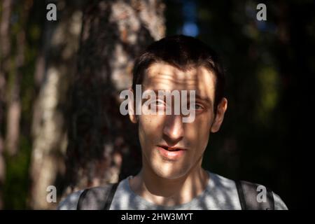 Porträt eines Mannes im Schatten der Blätter im Herbst. Sonniger Tag. Der Kerl posiert für ein Foto. Eine Person mit europäischem Aussehen. Ein interessanter Typ. Stockfoto