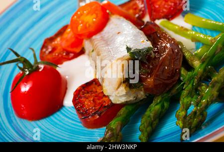 Gebackener Wittling mit sonnengetrockneten Tomaten, Spargel, cremiger Knoblauchsoße Stockfoto