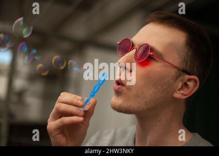 Der Mann lässt Seifenblasen aus. Der Typ freut sich jeden Tag. Ein junger Mann bläst und gibt Blasen frei. Stockfoto