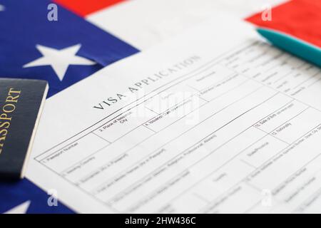 Frau, die das Antragsformular für das Visum ausgefüllt hat. Amerikanische Flagge auf dem Hintergrund. Einwanderung in die USA. Stockfoto