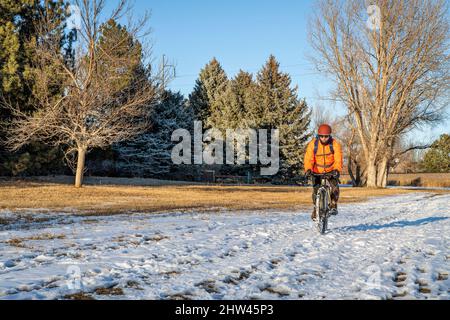 Älterer Radler, der im Winter auf einem schneebedeckten Trail in Fort Collins, Colorado, mit einem Tourenrad unterwegs ist Stockfoto