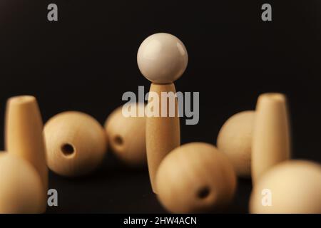 Holzkugeln und weiße Kugel auf Zylinder auf schwarzem Hintergrund, allein gegen alle, Nahaufnahme Stockfoto