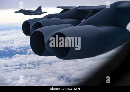 Ein schwedischer Saab JAS-39 Gripen-Kampfjet begleitet eine B-52H-Stratofortress, die während der Bomber Task Force England am 24. Februar 2022 dem Expeditionary Bomb Squadron 69., RAF Fairford, England, über Schweden zugewiesen wurde. Strategische Bombermissionen verbessern die Bereitschaft und das erforderliche Training, um auf potenzielle Krisen oder Herausforderungen auf der ganzen Welt zu reagieren. (USA Air Force Foto von Tech. Sgt. Corban Lundborg) Stockfoto