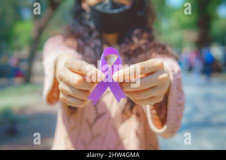 Frau auf der Straße mit einem violetten Band im Bewusstsein von Hodenkrebs, der jedes Jahr im April beobachtet wird. Stockfoto