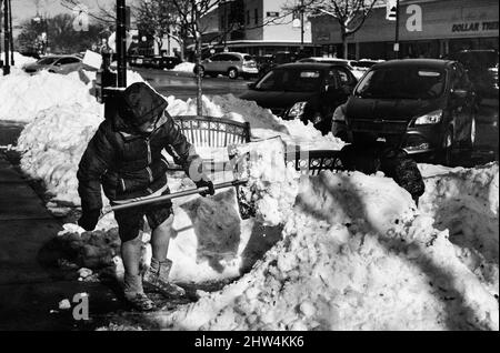 Ein junger Mann schaufelt nach einem Sturm Schnee vom Bürgersteig. Stockfoto