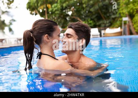 Heizen Sie sich im Pool auf. Aufnahme eines attraktiven jungen Paares, das sich in einem Pool nahe befindet. Stockfoto