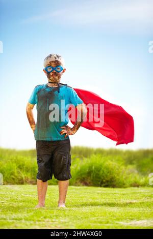 Kein Schmutz oder Schlamm wird mich verlangsamen. Porträt eines schlammigen kleinen Jungen, der wie ein Superheld verkleidet ist. Stockfoto