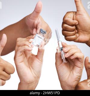 Sich selbst zu pflegen ist nicht egoistisch. Studioaufnahme einer Gruppe von Menschen, die Daumen nach oben zeigen und den Impfstoff vor grauem Hintergrund halten. Stockfoto
