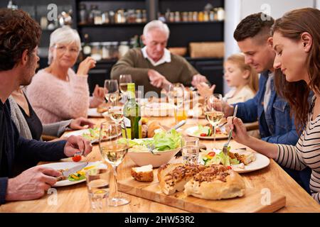 Trinken, essen und fröhlich sein. Eine kurze Aufnahme einer Familie, die am Esstisch ein Essen teilt. Stockfoto