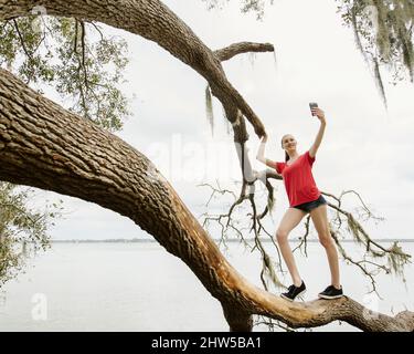 Athletin Frau, die Selfie auf einem Baum über dem Fluss nimmt Stockfoto