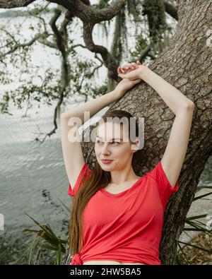 Lächelnde Frau, die sich gegen den Baumstamm lehnt Stockfoto