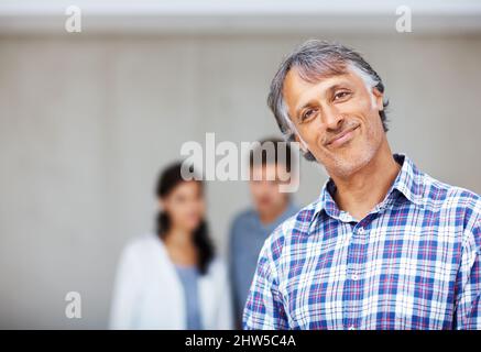 Reifer Architekt mit Paar im Hintergrund. Porträt eines reifen Architekten lächelnd mit Paar im Hintergrund. Stockfoto