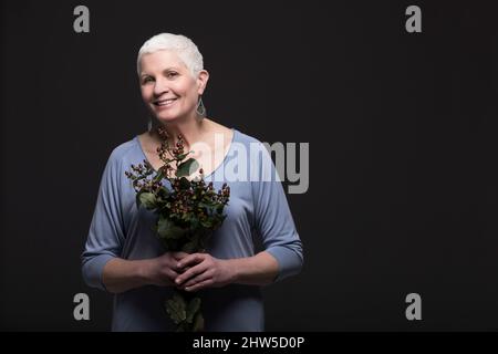 Studio-Porträt einer lächelnden Frau in blauem Hemd mit Blumenstrauß Stockfoto