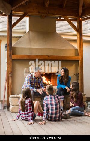 Familie mit Kindern (10-11, 12-13, 16-17) am Kamin sitzend Stockfoto