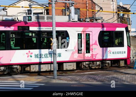 TOKIO, JAPAN - 3. März 2022: Eine Tokyo Sakura Tram (Toden Arakawa Line ), die an einem Bürgersteig im Tokioter Machiya-Gebiet vorbeifährt. Die Straßenbahn hat eine Werbung für Johoku Stockfoto