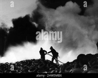 Fire at Tire Disposals Ltd, Thornliebank Industrial Estate, Glasgow, April 1968. Zwei Feuerwehrmänner stehen auf einem 25 Meter hohen Hügel aus lodernden Gummis ... und schwarzer Rauch wabert durch die Stadt. Stockfoto
