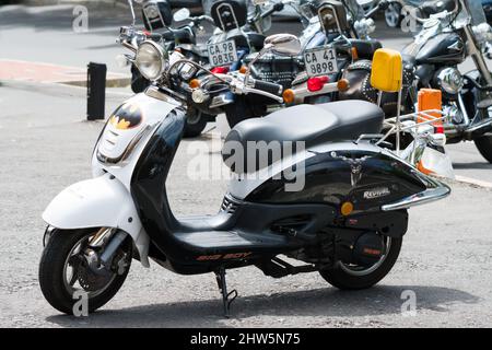 Scooter geparkt auf dem Bürgersteig mit Batman Aufkleber oder Aufkleber auf ihm und im Hintergrund Motorräder Stockfoto