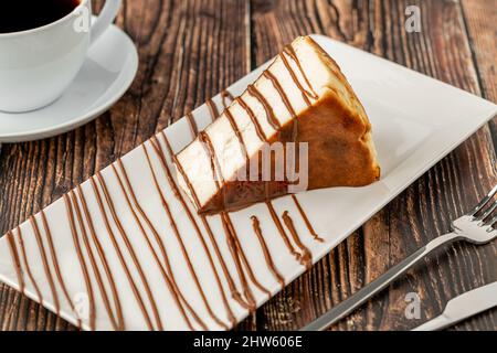 Geschnittener san sebastian Käsekuchen mit Kaffee auf Holztisch Stockfoto
