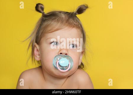 Porträt von niedlichen kaukasischen Kind Kind Mädchen von 2 Jahren mit Schnuller im Mund auf gelbem Hintergrund Stockfoto