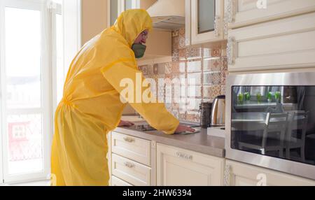 Ein Mann in Schutzkleidung reinigt und führt in der Küche in der Wohnung eine sanitäre Reinigung durch. Stockfoto