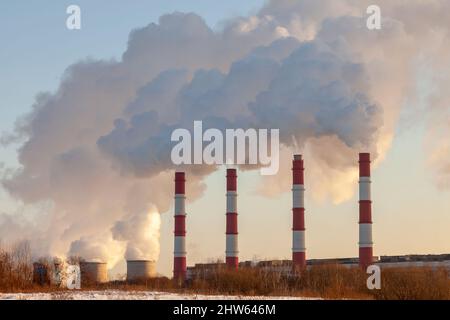 Eine Reihe von rauchenden Fabrikschornsteinen vor einem klaren Himmel. Stockfoto