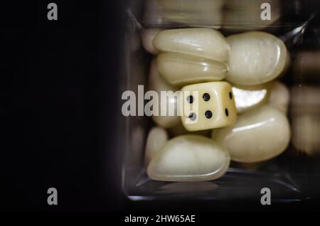 Weißer Iambic-Würfel aus Kunststoff in einer Glasflasche, umgeben von Kunststoffsteinen. Stockfoto