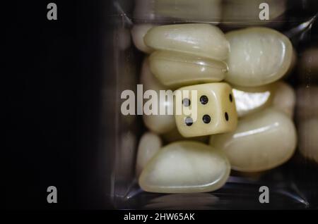 Weißer Iambic-Würfel aus Kunststoff in einer Glasflasche, umgeben von Kunststoffsteinen. Stockfoto