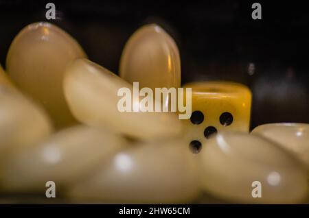 Weißer Iambic-Würfel aus Kunststoff in einer Glasflasche, umgeben von Kunststoffsteinen. Stockfoto
