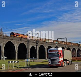 DB Cargo 66121 überquert das beeindruckende und massive Ditton Viadukt mit einem Güterzug, während ein Shuttleworth Scania-Lastwagen im Vordergrund vorbeifährt Stockfoto