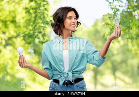 Lächelnde Frau, die verschiedene Glühbirnen vergleicht Stockfoto