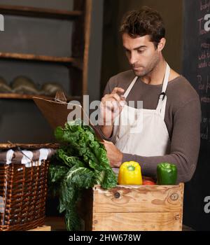 Vermisse ich etwas Ein junger Mann mit einem Klemmbrett, der neben einer Kiste voller Gemüse steht. Stockfoto
