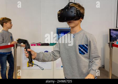 Acht Jahre Junge trägt VR-Headset, hält Controller in den Händen und genießen Sie neue Erfahrung in Videospielen. Spielstand auf der Messe der modernen tec Stockfoto